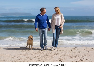 Romantic Mature Couple Walking On The Beach With Their Dog