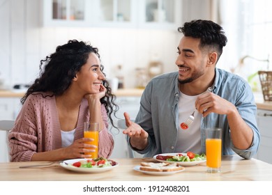 Romantic millennial arab couple eating tasty breakfast together in kitchen at home, enjoying delicious food and drinking orange juice, middle eastern spouses sitting at tabel chatting and laughing - Powered by Shutterstock