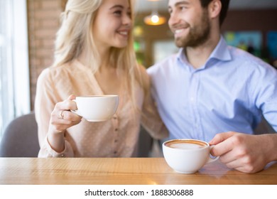 Romantic Millennial Couple Drinking Coffee And Looking At Each Other At Cozy Cafe, Selective Focus. Young Woman And Her Lover On Date At Restaurant, Enjoying Hot Beverage, Having Conversation