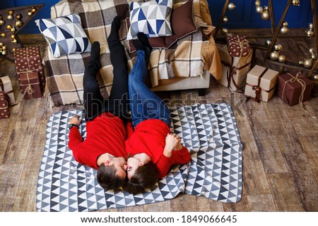 A romantic moment. A couple in red sweaters lies on the floor hugging and kiss