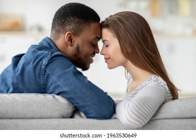 Romantic Moment. Loving Interracial Couple Bonding Together At Home, Affectionate Young Multicultural Lovers Holding Hands And Touching Foreheads While Sitting On Couch In Living Room, Closeup Shot - Powered by Shutterstock