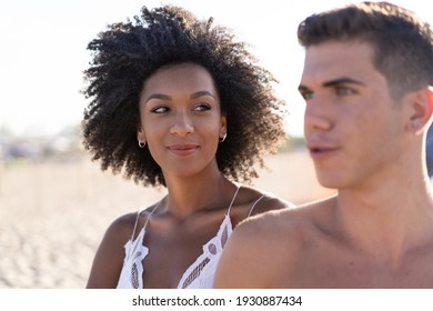 Romantic multiracial couple walking on the beach in the summer, close up on the face of the girl watching her boyfriend on vacation