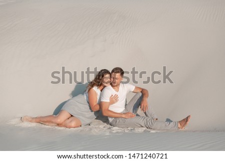 Romantic pair sit on white sand and huggins, in desert.