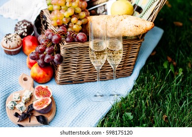 Romantic picnic at the park on a grass, delicious food: basket, wine, grapes, peaches, baguette, cupcakes, figs, cheese, blue tablecloth, two wineglass with champagne - Powered by Shutterstock