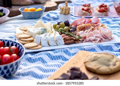 Romantic picnic setting in the garden, blue cloth and pillows. Fresh food, close up on cheese and meat platter, fruits and cookies around it. Outdoor relaxing concept, fresh air eating - Powered by Shutterstock