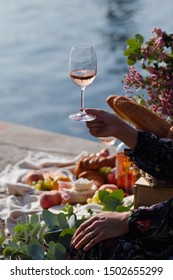 Romantic Picnic For Two On The Quay Of Seine River In Paris. Parisien Elegancy And Chic. Traditional French Croissants, Cheese, Fruits And Glasses Of Wine. Young Girl Holding Glass Of Wine In Her Hand