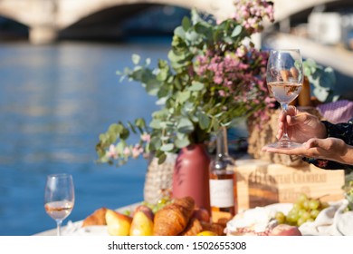 Romantic Picnic For Two On The Quay Of Seine River In Paris. Parisien Elegancy And Chic. Traditional French Croissants, Cheese, Fruits And Glasses Of Wine. Young Girl Holding Glass Of Wine In Her Hand