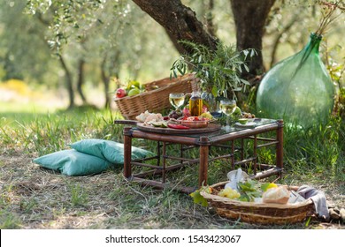 Romantic picnic under olive tree. Delicious italian meal served on a wooden table. Baskets with food, branches in glass jar. Sunny autumn day. Italy, Tuscany - Powered by Shutterstock