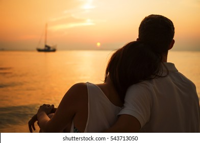 Romantic portrait of attractive couple in love hugs sitting on the beach at the sunset on  tropic island. Against the backdrop of the sea and setting sun. In the distance a boat in the sea. Silhouette