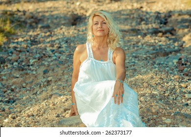 Romantic Portrait Of A Beautiful Older Woman. Mature Beautiful Blonde In A White Dress Walks On The  Road 