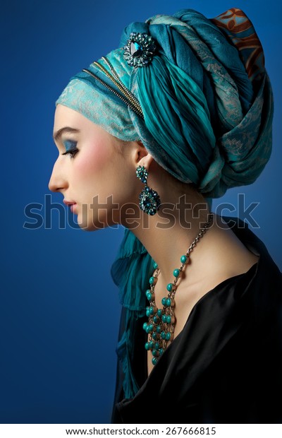 Romantic portrait of young woman in\
a turquoise turban with jewelry on a beautiful\
background