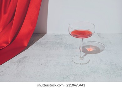 Romantic Red Composition With Wine Party Glass And Red Satin Curtain On Marble Background. Modern Minimal Aesthetic.