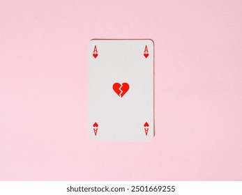 Romantic relationship problems and breakup. Divorce. Ending love. Ace of hearts playing card is lying on a pink surface and showing a broken heart in the middle.