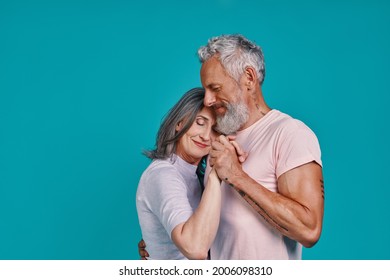 Romantic senior couple dancing and smiling while standing together against blue background - Powered by Shutterstock