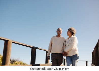 Romantic senior couple holding hands and smiling while taking a walk along a wooden foot bridge. Affectionate elderly couple enjoying a refreshing beach holiday after retirement. - Powered by Shutterstock