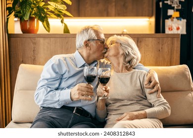 A romantic senior couple is kissing and toasting with wine at home. - Powered by Shutterstock