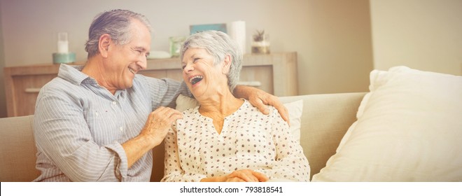 Romántica pareja de ancianos riéndose mientras se sientan en el sofá en casa