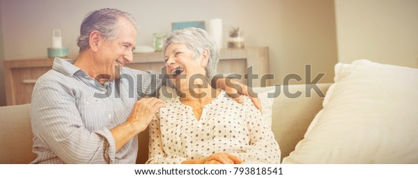 Romantic senior couple laughing while sitting on\
sofa at home
