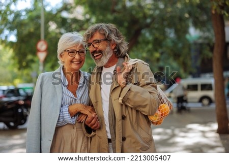A romantic senior couple is outdoors in the city taking a walk after shopping fruit in the market.