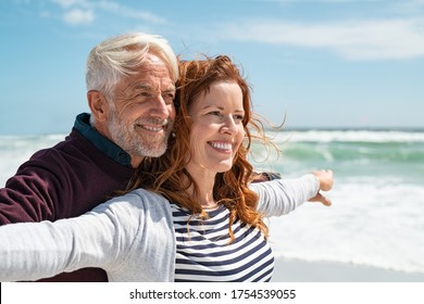 Romantic senior couple with outstretched arms enjoying vacation. Old husband embracing from behind beautiful wife at sea. Happy smiling mature couple carefree: future, imagination and contemplation. - Powered by Shutterstock