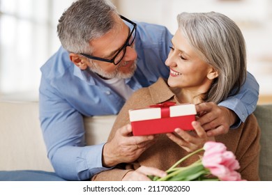 Romantic senior man congratulating happy wife on Valentines Day or March 8 at home, surprised elderly female receiving gift box with red bow and tulips bouquet from loving husband. Selective focus - Powered by Shutterstock