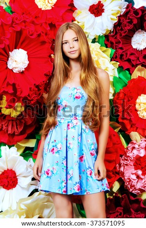 Romantic smiling girl posing in summer dress by a background of bright paper flowers. Beauty, fashion.