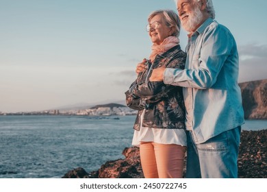Romantic smiling senior couple hugging on the rocky beach at sea enjoying vacation and retirement looking at horizon over water - Powered by Shutterstock