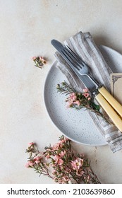 Romantic Or Spring Table Setting. Knife And Fork, Little Pink Flowers And Linen Napkin On A Plate, Light Concrete Background. Flat Lay.