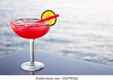 Romantic strawberry margarita cocktail served against an ocean background.