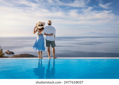 A romantic summer holiday couple stands at the edge of an infinity swimming pool and enjoys the view over the ocean - Powered by Shutterstock