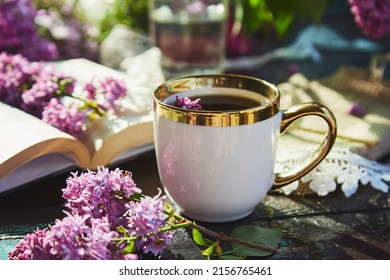 Romantic sunny garden, relax and leisure with cup of coffee. Mock up white cup and book surrounded lilac flowers. Cup of coffee, lilac flowers and book. Hard shadows. Summer days, aesthetic garden.