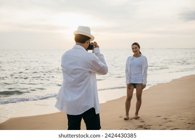 Romantic sunrise at beach for young couple in white as boyfriend takes candid photos of his girlfriend. blissful moment of togetherness filled with love and joy against backdrop of ocean. - Powered by Shutterstock