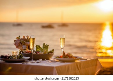 Romantic sunset dinner on the beach. Table honeymoon set for two with luxurious food, glasses of champagne drinks in a restaurant with sea view. Summer love, romance date on vacation concept.