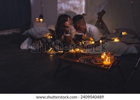 Romantic surprise for girlfriend or boyfriend. Bedroom prepared for watching old movies with popcorn, decorated with lights and candles. Cozy home Christmas atmosphere, hot chocolate with marshmallow