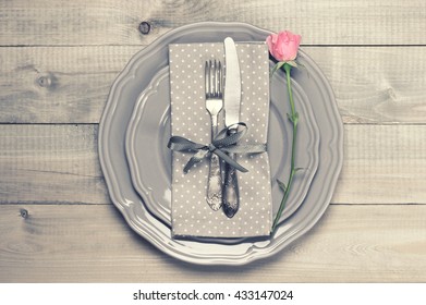 Romantic table setting: grey plates, vintage fork and knife, napkin and pink rose on rustic wooden table. Top view point. - Powered by Shutterstock