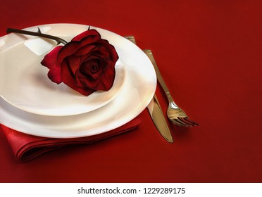 Romantic Table Setting For Valentines Day Or Dinner Date Celebration Wedding Restaurant . Valentines Day Table Setting With Red Rose Bud, White Plates, Fork And Knife On Red Tablecloth Background. 