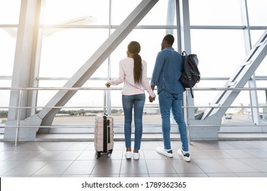 Romantic Travel. Black Couple In Love Looking At Window In Airport, Holding Hands And Smiling, Ready To Honeymoon Trip, Rear View With Copy Space