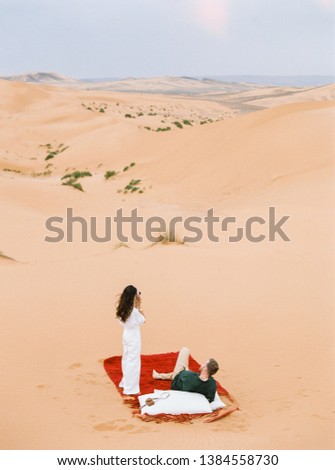 Romantic traveler taking photo on Sahara desert. Young couple enjoying the sunset in dunes. Adventure travel lifestyle concept.