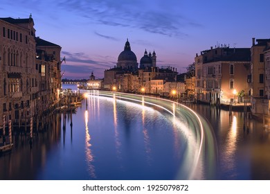 Romantic Venice at night. Cityscape image of Grand Canal in Venice, with Santa Maria della Salute Basilica reflected in calm sea. Lights of passenger boat on the water.