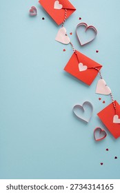 Romantic vertical composition features red envelopes strung along twine with pastel heart cutouts, scattered small hearts on a soft blue background