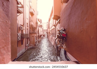 A romantic view from a window festooned with padlocks, overlooking the tranquil Canale delle Moline as it meanders through the heart of Bologna