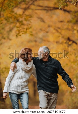 Romantic walk through fall forest by senior couple.