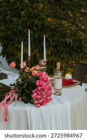 Romantic wedding or proposal table decor with roses, candles and wine outdoors. Elegant floral arrangement, intimate atmosphere, celebration setup, love story mood, no people, natural light scene calm