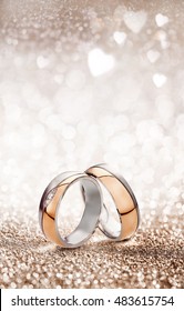 Romantic wedding ring celebration background with two gold rings balancing upright over a light sparkling background with white hearts and copy space for an invitation or greeting card