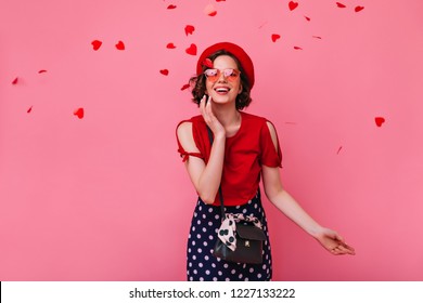 Romantic white woman with brown hair expressing happiness in valentine's day. Enchanting stylish girl in funny glasses posing on rosy background with confetti.