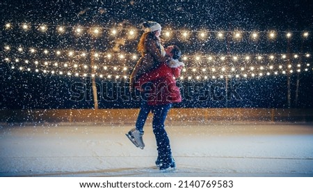 Romantic Winter Snowy Evening: Ice Skating Couple Meeton on Ice Rink and Have Fun. Pair Skating Boyfrined Lifts His Beautiful Girlfriend and Spins. Love, Dance, Embrace, Figure Skate. Wide Shot