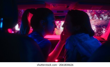 Romantic Young Adult Lesbian Female Couple Kiss On The Front Seat Of Their Car On A Rainy Night In The City. Women In Love On A Date In Neon Urban Environment. Concept Of LGBT, Relations And Driving.