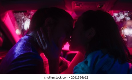 Romantic Young Adult Lesbian Female Couple Kiss On The Front Seat Of Their Car On A Rainy Night In The City. Women In Love On A Date In Neon Urban Environment. Concept Of LGBT, Relations And Driving.