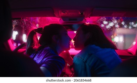 Romantic Young Adult Lesbian Female Couple Kiss on the Front Seat of Their Car on a Rainy Night in the City. Women in Love on a Date in Neon Urban Environment. Concept of LGBT, Relations and Driving.