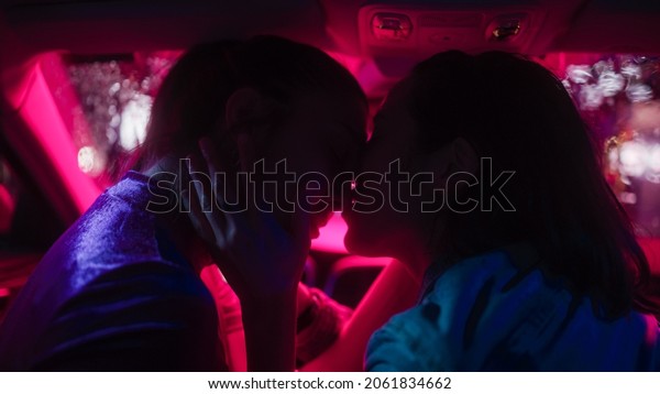 Romantic Young Adult Lesbian Female Couple Kiss\
on the Front Seat of Their Car on a Rainy Night in the City. Women\
in Love on a Date in Neon Urban Environment. Concept of LGBT,\
Relations and Driving.